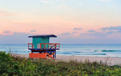 Colorful lifeguard tower on a beach at sunset, overlooking the ocean waves and coastal vegetation, representing a relaxed coastal community in Georgia.