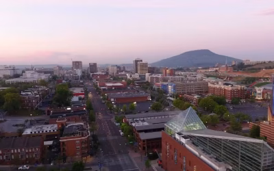Aerial view of downtown Chattanooga, Tennessee, showcasing urban landscape, buildings, and Lookout Mountain in the background at sunset.